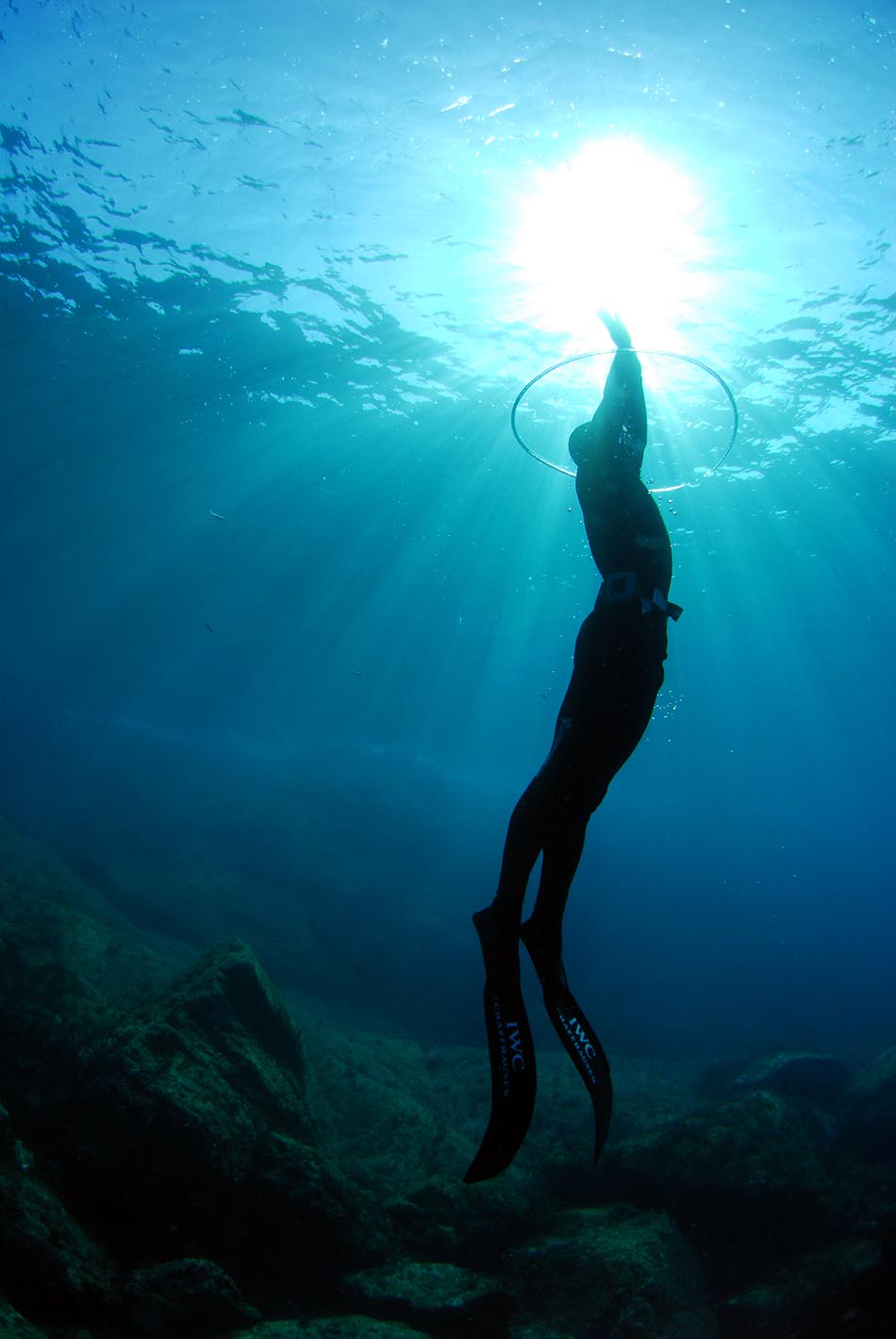 Apnoetaucher steigt zur Oberfläche auf, beleuchtet von den Sonnenstrahlen unter Wasser.