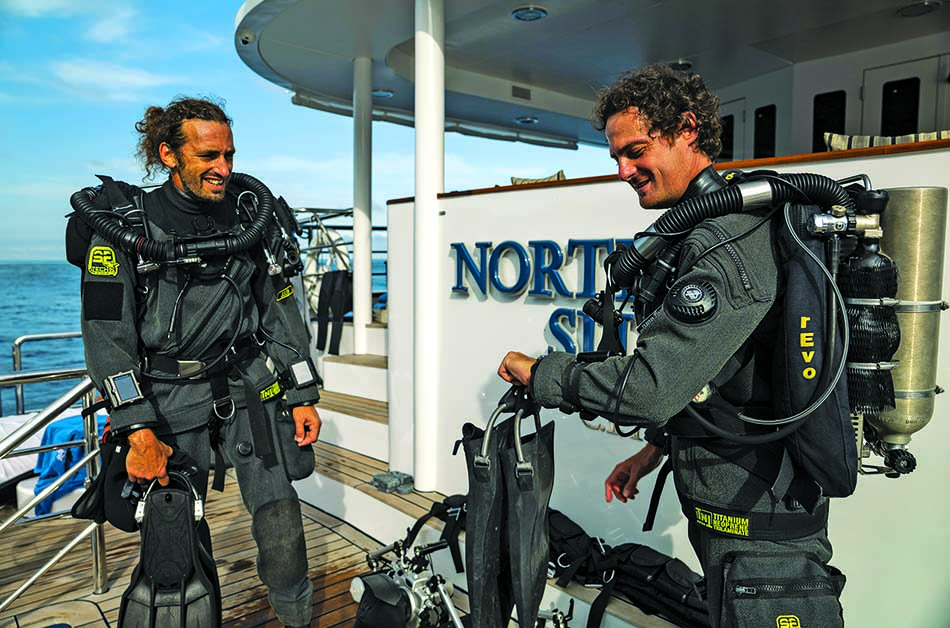 Zwei Taucher in Anzügen bereiten ihre Ausrüstung auf einem Boot vor, das für die Unterwassererkundung bestimmt ist.